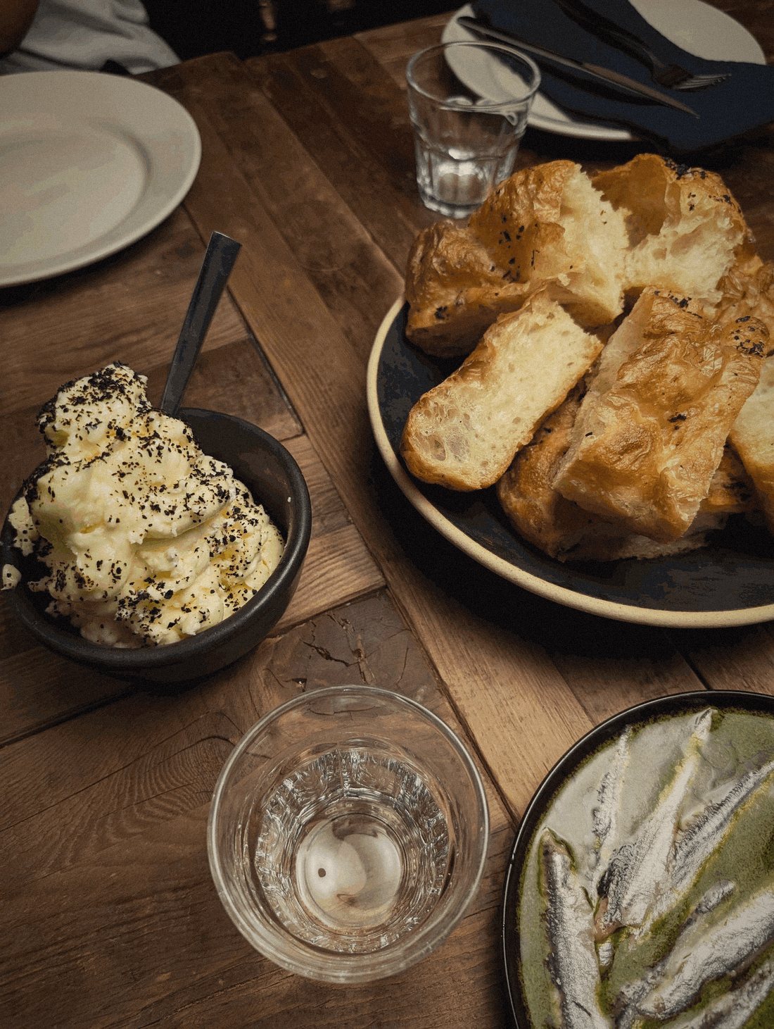Bread, whipped butter, and anchovies on a wooden table